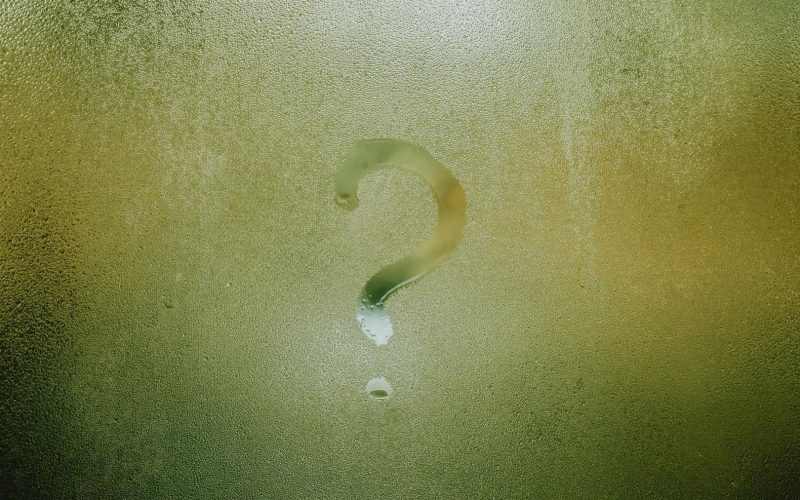 Frågetecken ritat i kondens på en grönaktig yta, symboliserar obesvarade frågor.